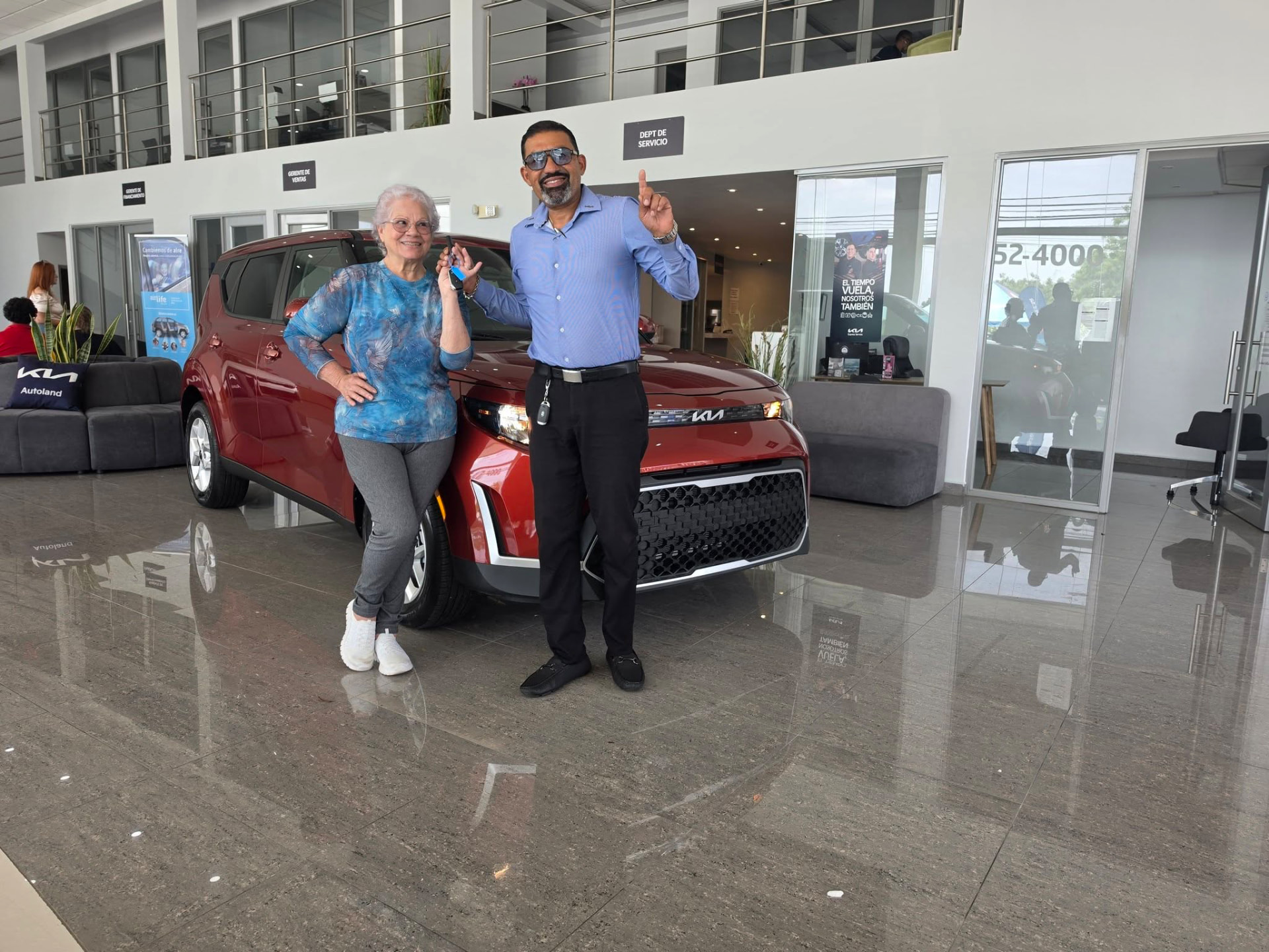 Ricardo junto a una clienta y un KIA Soul rojo en el concesionario